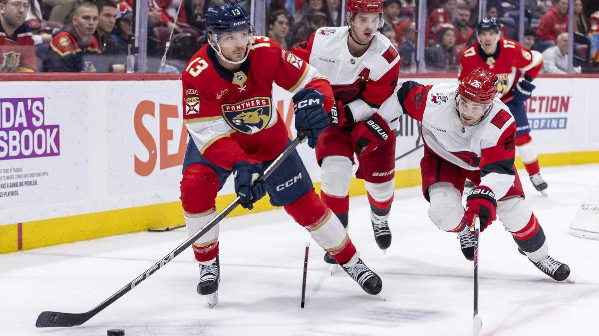 Florida Panthers center Sam Reinhart (13) looks to pass the puck as Carolina Hurricanes defenseman Sean Walker (26) and center Sebastian Aho (20) defend in the third period of their NHL game at Amerant Bank Arena on Friday, Dec. 19, 2025, in Sunrise, Fla.