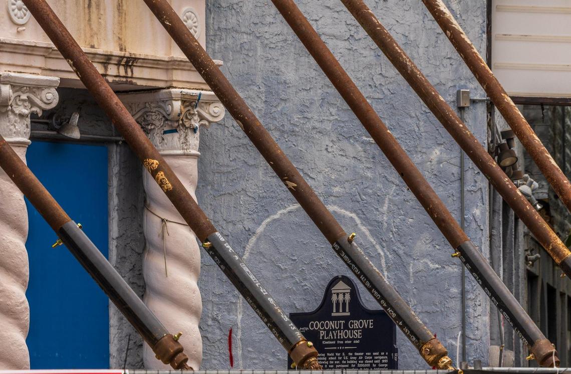 Steel braces support the front of the Coconut Grove Playhouse along Main Highway, where a sign tells the history of the iconic theater. The beams were installed to stabilize the building after a contractor’s error during interior demolition work in preparation for renovation left the structure at risk of collapse.