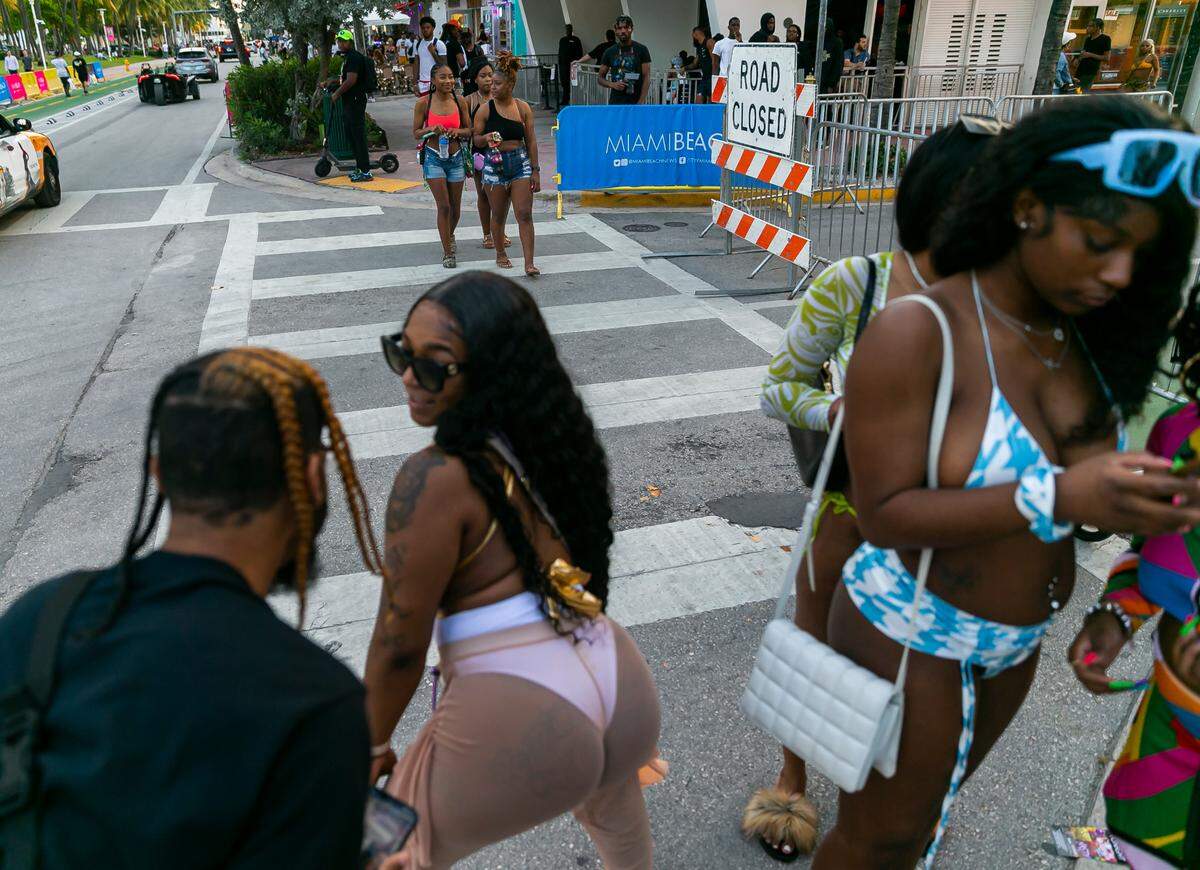 A woman twerks as people walk past in Miami Beach, Florida on Friday, March 25, 2022. City officials imposed a midnight curfew and forced stores to stop selling alcohol after 6 p.m. The restrictions were set in place after two shootings in Miami Beach the weekend before caused city officials to announce a “state of emergency.”