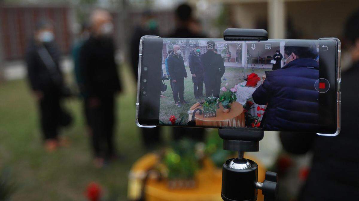 A worker livestreams a funeral ceremony for family members who could not attend a burial at cemetery amid the coronavirus outbreak.