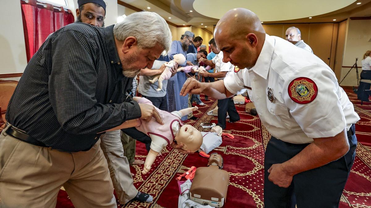 Jorge Anzardo, bombero de Miami-Dade, muestra a Jamil Rizvi cómo realizar compresiones torácicas de reanimación cardiopulmonar en un maniquí infantil durante una sesión de capacitación sobre cómo responder a emergencias médicas en el Centro Islámico del Gran Miami-Masjid, en Miami Gardens, Florida, martes 27 de junio de 2023.