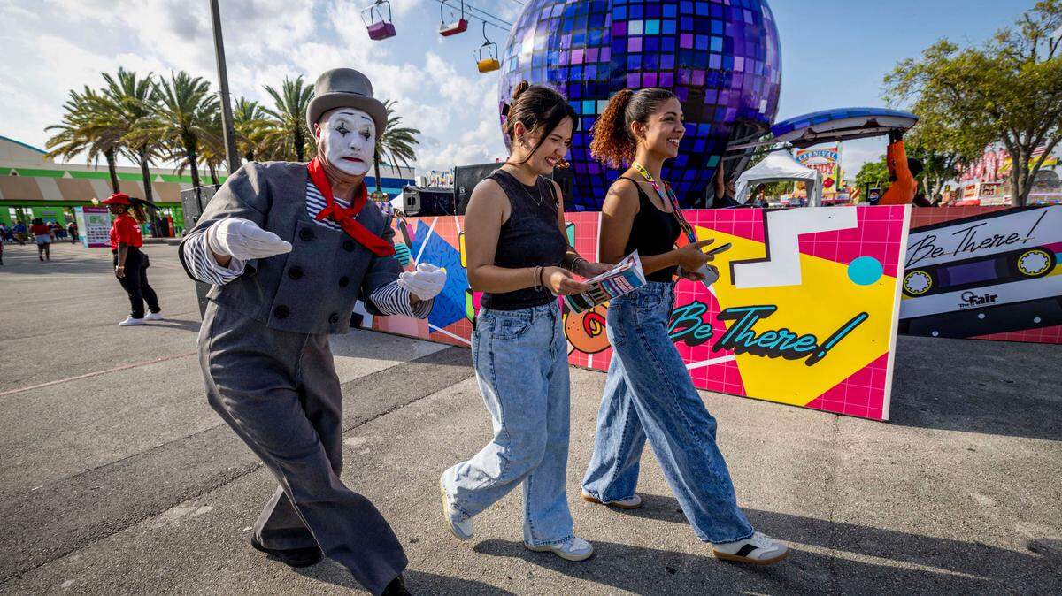 Two young ladies share a laugh as they are followed by a mime at the Miami-Dade County Fair & Exposition