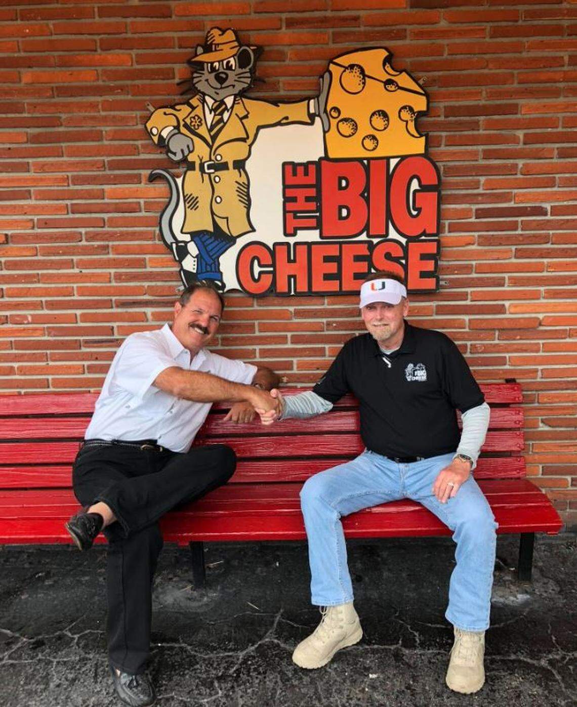 Garry Duell Jr. and Bill Archer share a handshake on the bench of the restaurant they founded in 1984, The Big Cheese, in an undated photo.