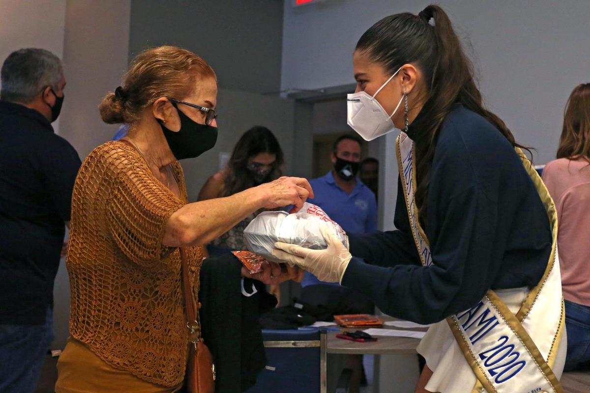Miss Carnaval Miami 2020 Valeria Uzc‡tegui, 17, hands out a meal to Julia Guerra, 71, during a Thanksgiving meal distribution event for senior residents at Smathers Plaza II organized by the Kiwanis Club of Little Havana in Miami, Florida, on Thursday, November 26, 2020.