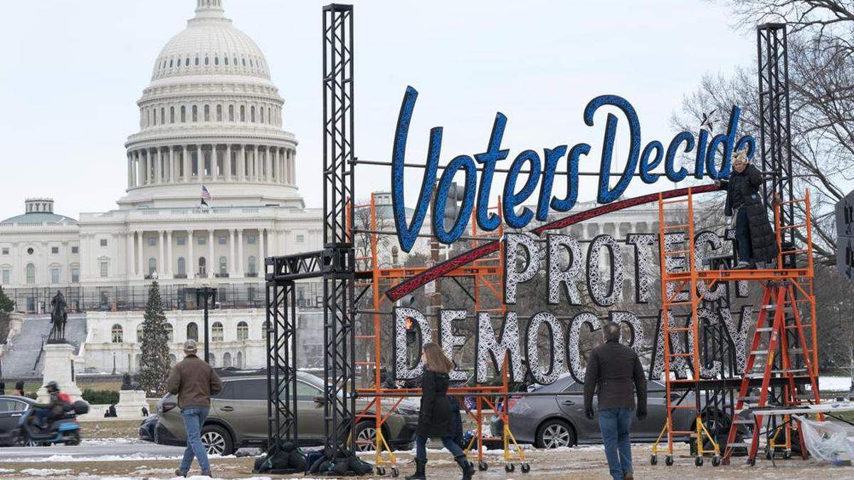 Con el Capitolio de Estados Unidos de fondo, la gente pasa por delante de un cartel el 6 de enero de 2022 que dice "Los electores deciden proteger la democracia".