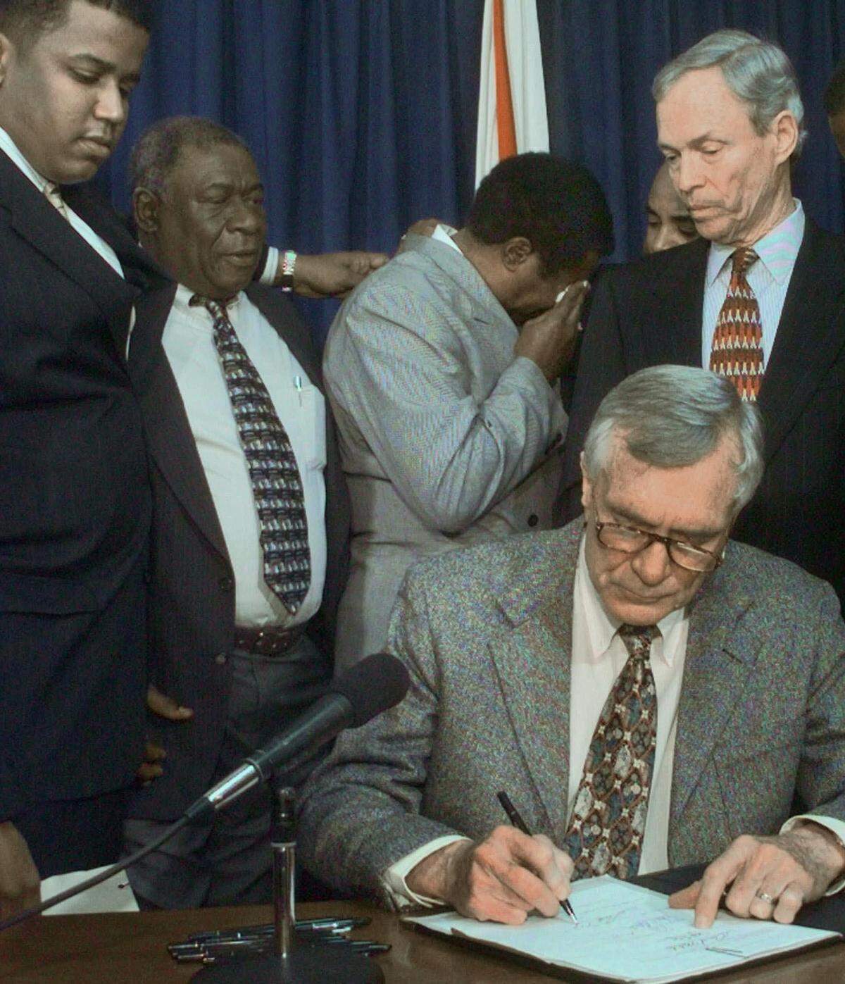 As former Florida Gov. Lawton Chiles signs their claims bill, an emotional Wilbert Lee breaks into tears on the shoulder of then-Lt. Gov. Buddy MacKay, right, on May 1, 1998, in Tallahassee, Florida. Rep. Kendrick Meek, D-Miami, left, and Freddie Pitts, second from left, watch the signing. Pitts and Lee, pardoned after 12 years in prison for murders they maintain they did not commit, will receive $500,000 each after an administrative law judge decides to release the compensation.