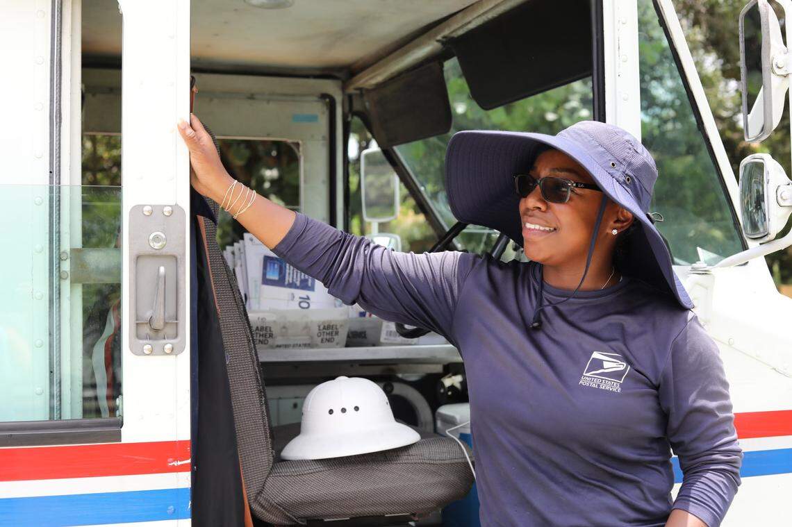 Olivia Gordon, a mail carrier for the United States Postal Service, stands for a portrait alongside her un-air-conditioned mail truck, wearing the floppy hat and long-sleeved shirt that keeps her out of the sun, on July 5, 2023.