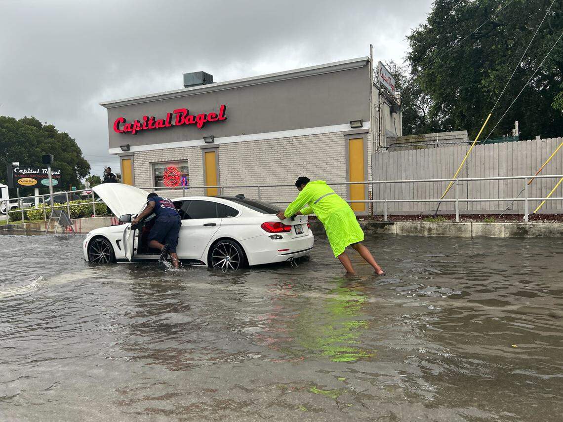 Two people push a car through a flooded Commercial Blvd. near Capital Bagel on Andrews Ave. in Oakland Park on Friday, Oct. 10, 2025. (Sienna Cavaretta/Courtesy)