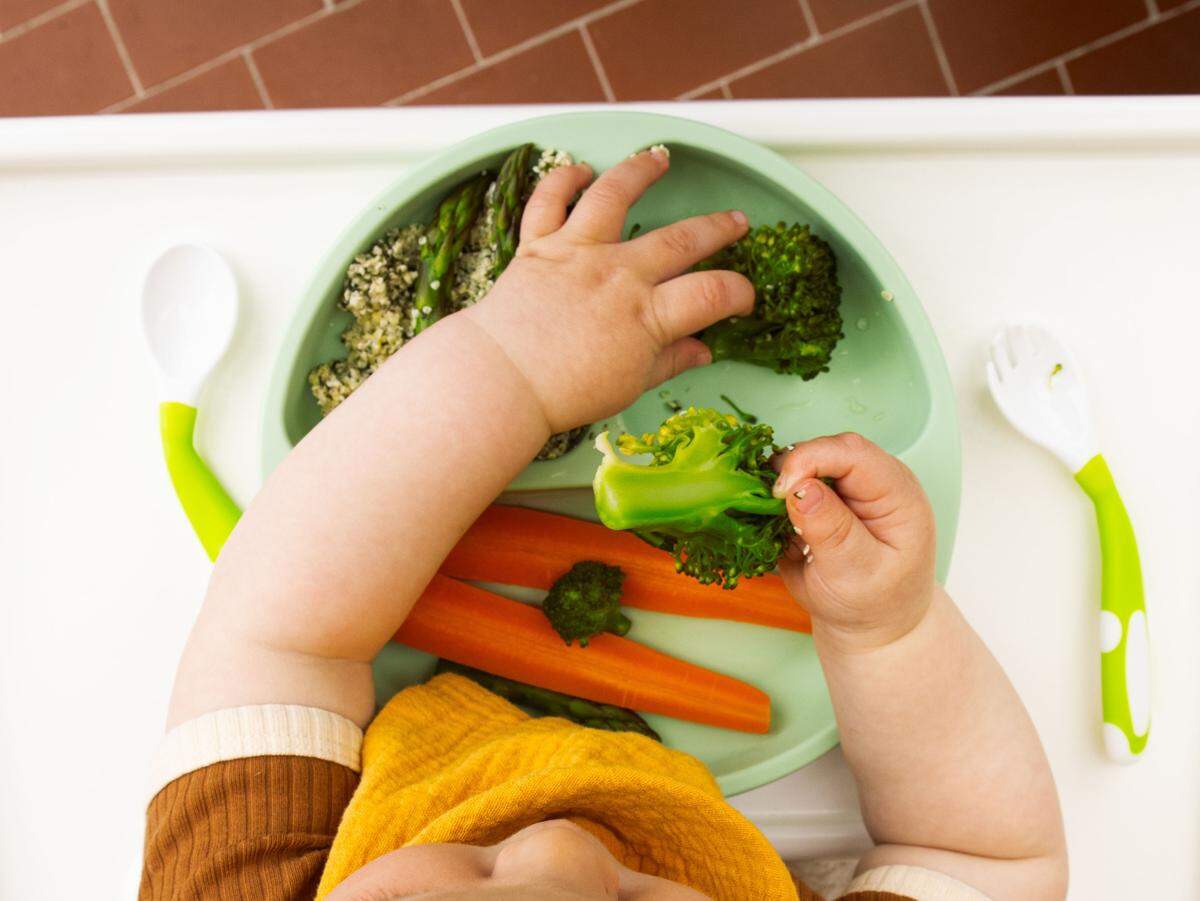baby eating vegetables off plate