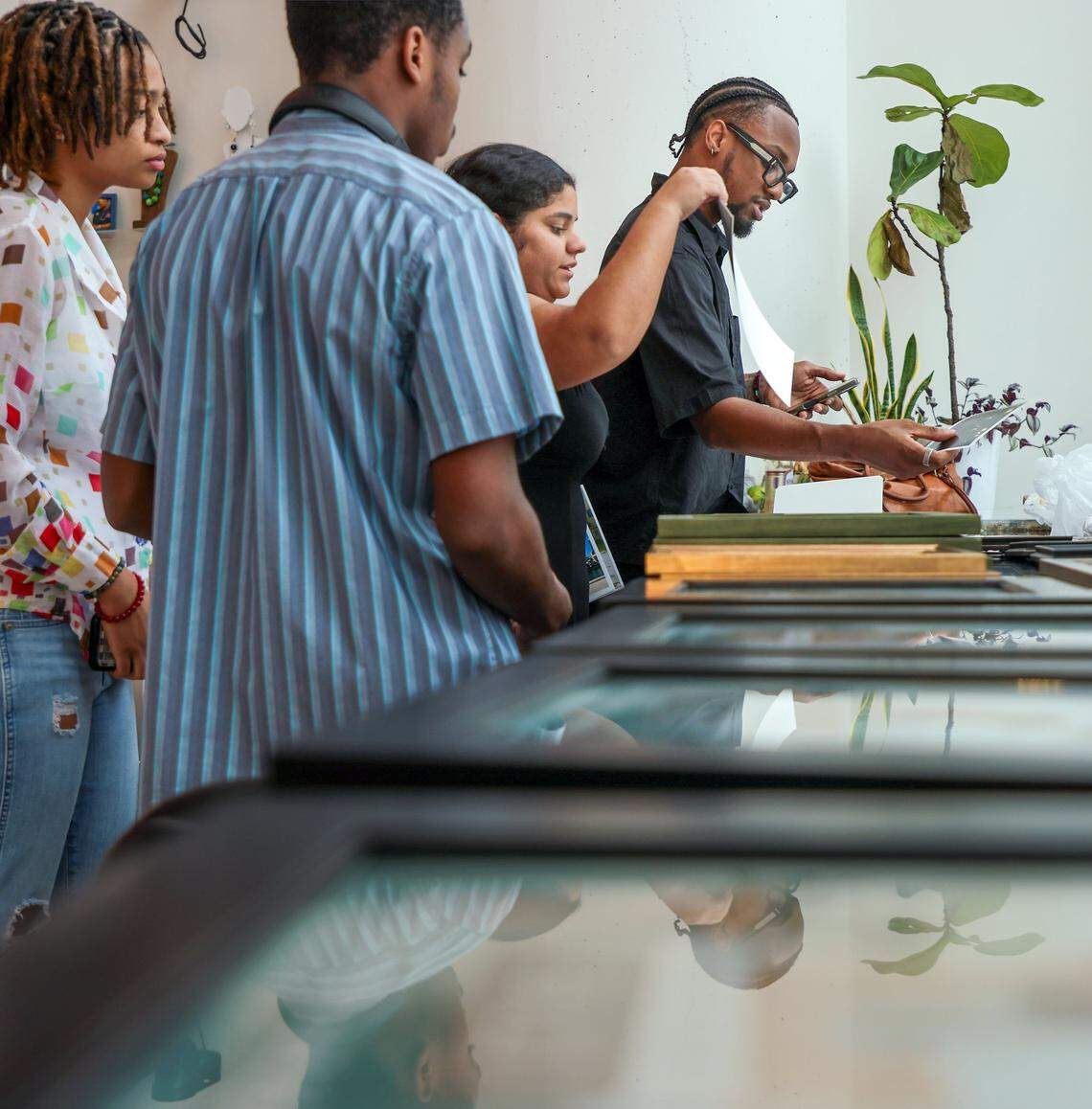 Curators Shayna Lewertow, 17, left, Alford Archer, 15, and Hannah Cabrera, 17, begin framing the artwork for installation with help from Nyya Toussaint, right. Four high school students installed photos inside the First Church Miami coffee shop for the exhibition Sparrow, featuring the photography of local photographers navigating homelessness under the artistic direction of Miami-based artist Christopher Mitchell on Sunday, November 30, 2025.