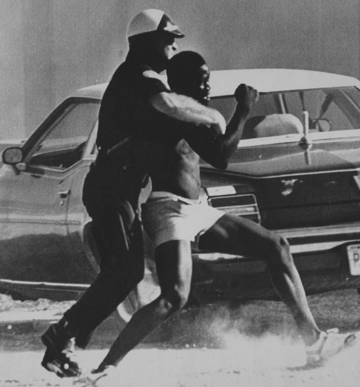 In this May 19, 1980 file photo, a Miami police officer is seen tackling a man they say was trying to loot a Zayre’s store on Northwest 54th Street after violence erupted in the wake of a trial that found four Miami police offers innocent in the beating death of Arthur McDuffie.