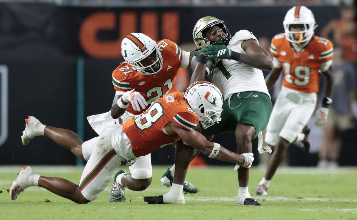 Miami Hurricanes defensive lineman Armondo Blount (18) and linebacker Jaylin Alderman (21) take down South Florida Bulls tight end Jonathan Echols (1) in the second half of their NCAA football game at Hard Rock Stadium in Miami Gardens, Florida, on Saturday, September 13, 2025.