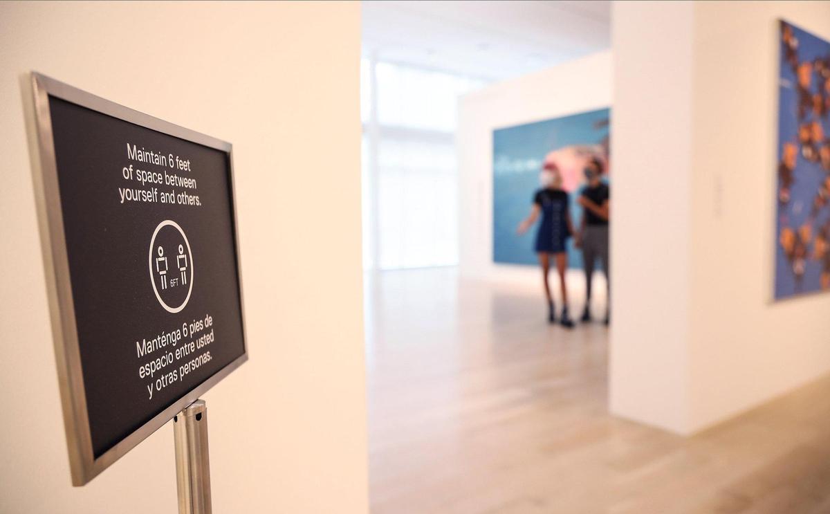 A sign reminds visitors to practice social distancing as Vincent Electra, 23, left, (that is name she provided), and Doug Giraldo, 25, right, cruise through Tomas Esson’s exhibition “The GOAT” while wearing masks on members opening day on Wednesday, September 2, 2020 in Miami’s Design District.