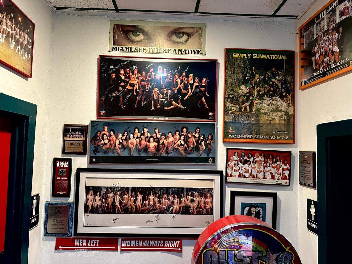 The bathroom wall at The Big Cheese seen here on March 5, 2025, is a continuation of the wall of fame with UM and other sports’ team’s memorabilia and the famed “Miami. See It Like a Native” ad poster from the late-’70s and early-’80s. It’s also a nod to founders’ Bill Archer and Garry Duell Jr.’s sense of humor. Note the signs pointing to the men’s and women’s rooms.