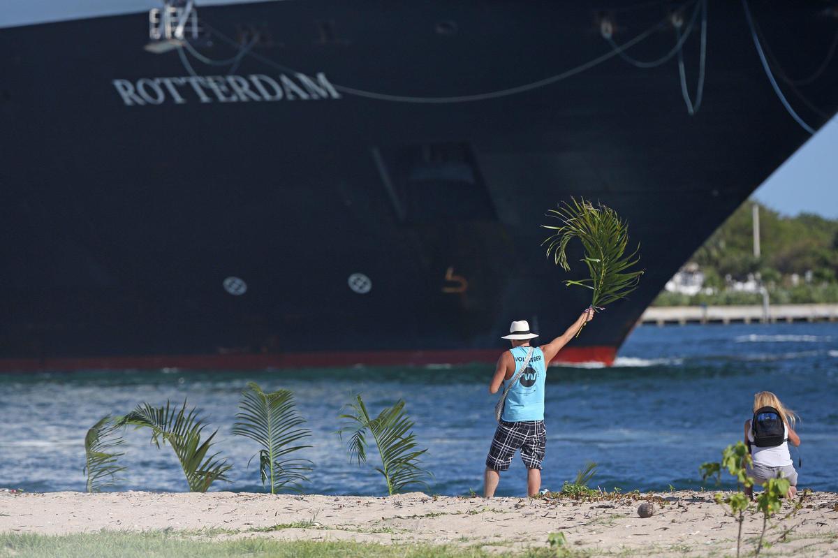 A man on the beach waves a palm frond in the air to welcome the Rotterdam and its passengers and crew into Port Everglades on Thursday, April 2, 2020. The Rotterdam followed its sister ship, the Zaandam into port. The Zaandam had COVID-19 passengers on board and sailed at sea for 12 days searching for a place to dock.