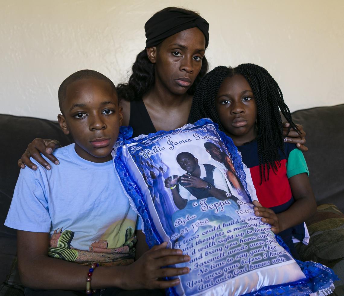 Jahkari Gordon, 12, left, Sophia Gilbert, 34, and Samya Gordon, 7, right, hold a memorial pillow of the late Willie James Gordon at their home in Miami’s Model City neighborhood on Saturday, Dec 7, 2019. Gordon, the children’s father and Gilbert’s boyfriend, was fatally shot six years ago. Gilbert has struggled to support her family while working at her children’s charter school.