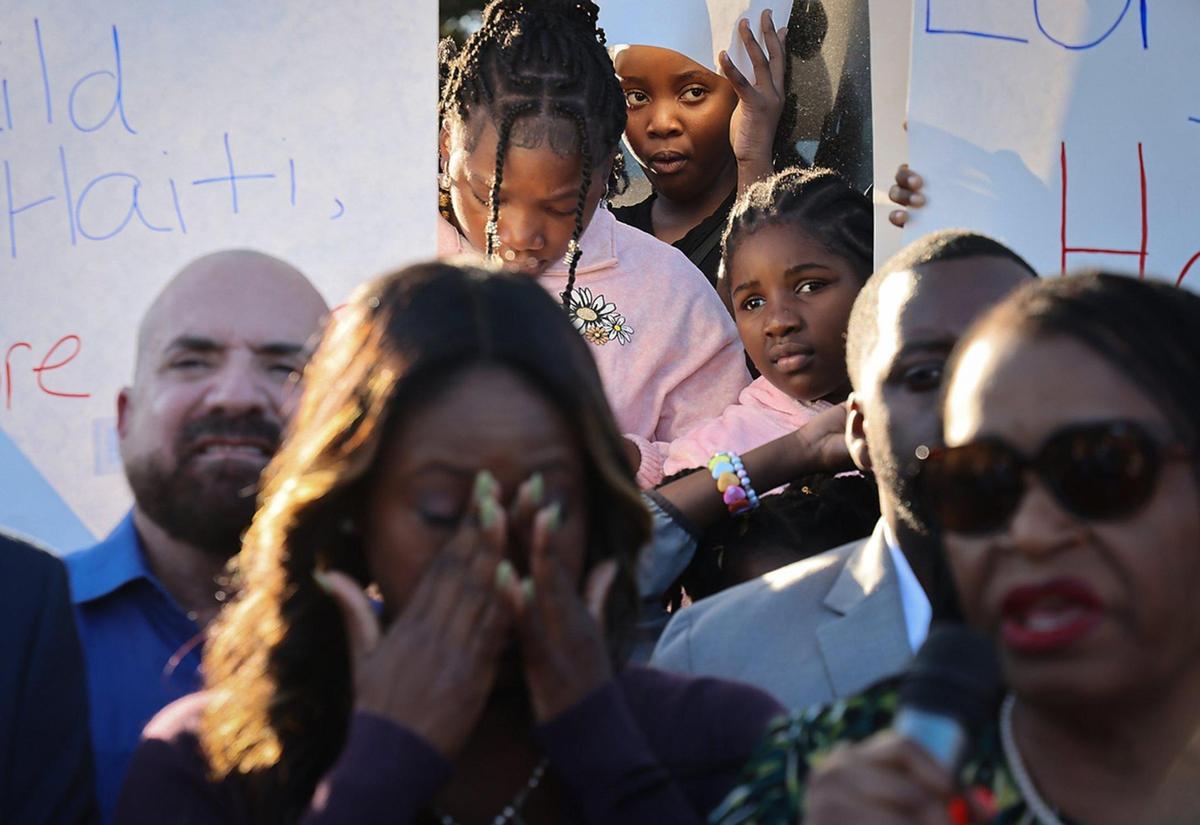 Children gaze beyond signs as members of the Haitian community and others gathered at Toussaint L’ Ouverture Statue for the customary moment of silence occurring at 4:53PM – the time of the 2010 earthquake prior to leading a procession to the Little Haiti Cultural Complex for a ceremonial remembrance of those who perished on Sunday, December 12, 2025.