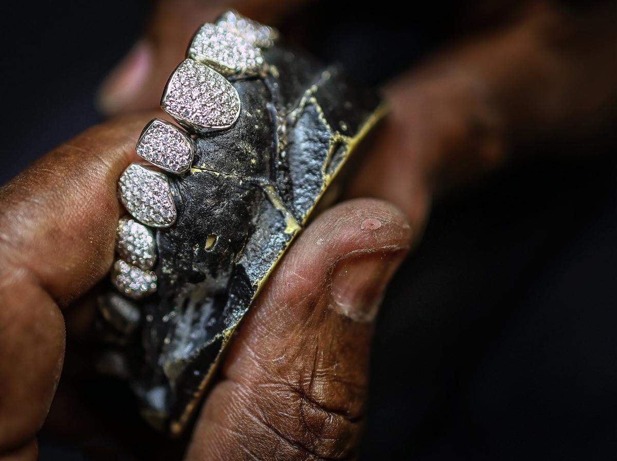 Lando Plein, 63, and son Philip operate Lando Golds, who pioneered the custom gold grillz industry after bringing his talents from New York City to Miami, Florida, forty years ago. Lando checks his artistry of gold and diamond teeth inside Lando Golds in Miami, Florida, on Wednesday, July 30, 2025.