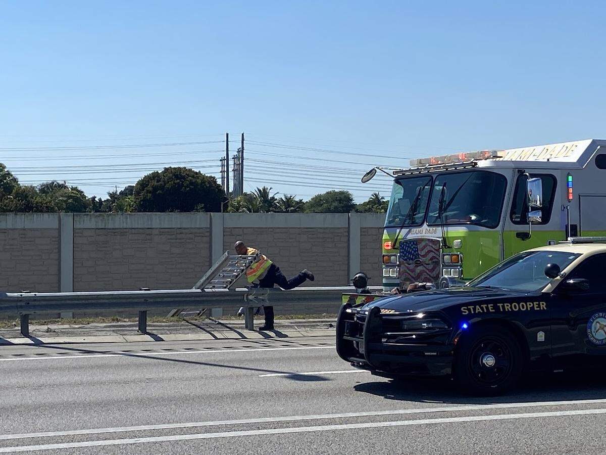 A Miami-Dade Fire Rescue firefighter climbs over a barrier on the shoulder of the Florida Turnpike near Princeton Friday, Feb. 28, 2025. Divers had just rescued a driver whose car went into a canal under the highway.