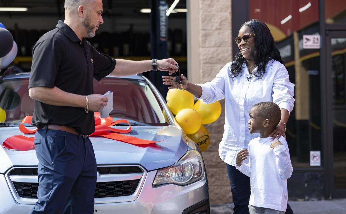 Renee King, 36, and her son Kingston Allen, 4, receive a pair of keys to a free refurbished Subaru Impreza by Yoel Victores, 42, a franchise owner of a Midas, at his shop on Thursday, Feb. 12, 2026, in Fort Lauderdale, Fla. King, a single mom with two children, was forced to give up her previous car and relied entirely on public transportation to get to work.