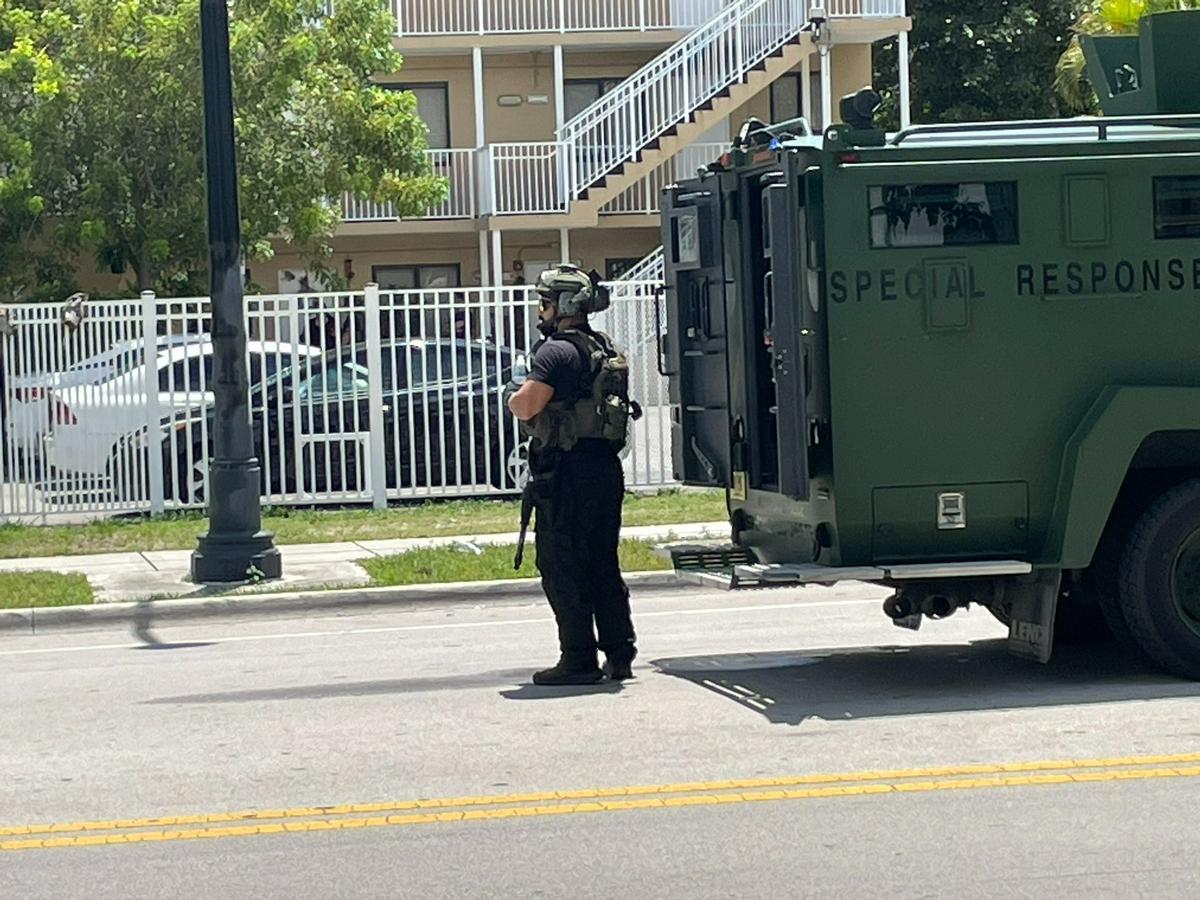 A Miami-Dade County police officer with a rifle takes up a post on Southwest 27th Avenue, near Bird Avenue, in Coconut Grove shortly after noon on Friday, July 22, 2022. Police descended on the Miami neighborhood while pursuing two people suspected of a shooting in Coral Gables.