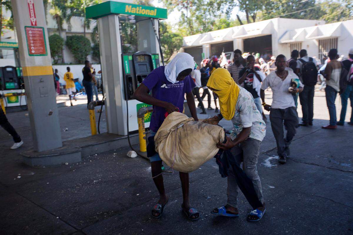 Masked protesters carry off a sack filled with looted items, during a protest demanding the resignation of President Jovenel Moise in Port-au-Prince, Haiti, Monday, Feb. 11, 2019. Protesters are angry about skyrocketing inflation and the government’s failure to prosecute embezzlement from a multi-billion Venezuelan program that sent discounted oil to Haiti. (AP Photo/Dieu Nalio Chery)