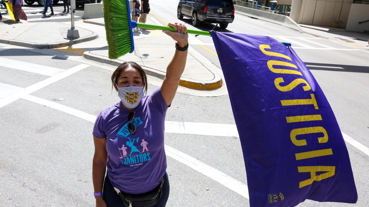 Alise Rosario, union organizer at 32BJ SEIU, raises a broom with a flag during a march in downtown Miami in protest over alleged intimidation and retaliation over union organizing and unsafe working conditions for janitors, Thursday, February 11, 2021.