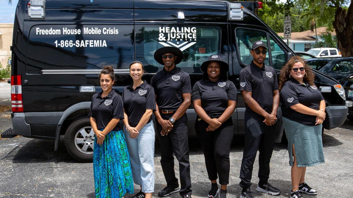 Miembros del Centro de Sanación y Justicia frente al van de respuesta a crisis y atención urgente gratis de Freedom House en Liberty City, Florida, el miércoles 8 de junio de 2022. El programa insta a los negros e hispanos a llamar al 1-866-SAFEMIA en caso de una emergencia de salud mental en lugar de llamar al 911.