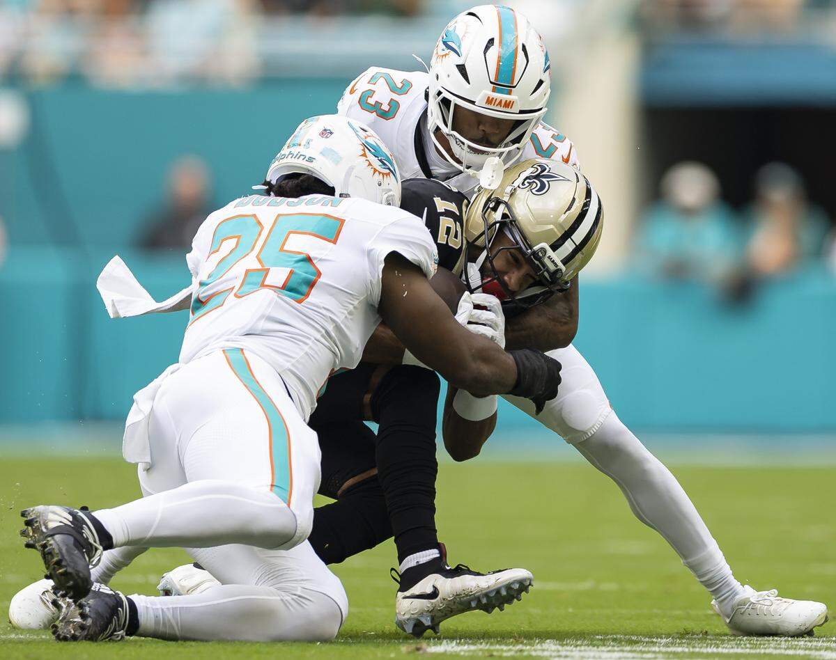 New Orleans Saints wide receiver Chris Olave (12) is tackled by Miami Dolphins linebacker Tyrel Dodson (25) and cornerback Jack Jones (23) in the first half of their NFL game at Hard Rock Stadium on Sunday, Nov. 30, 2025, in Miami Gardens, Fla.