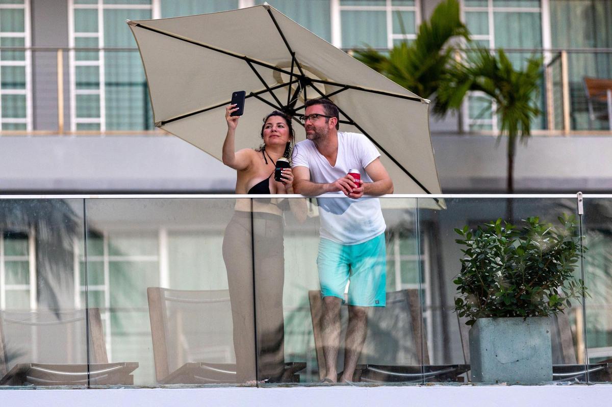 A man and woman take a selfie from the Hotel Victor South Beach rofftop terrace overlooking Ocean Drive during Memorial Day weekend at Miami Beach, Florida, on Sunday, May 28, 2023.