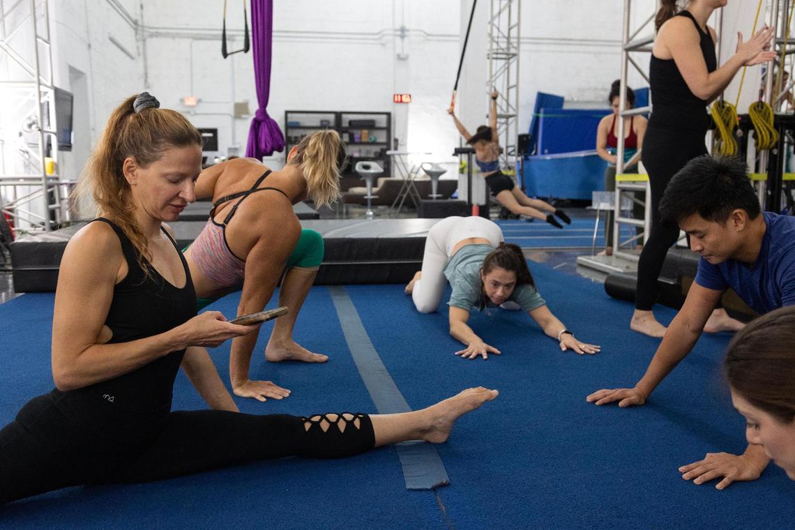 Mila Puletti checks her phone while stretching with her students during the beginning of an adults silks class at the Miami Circus Arts Center on Aug. 19, 2023, in Miami, Fla. Puletti trains and teaches full-time, though she is looking to get into real estate as a side job to help pay bills.