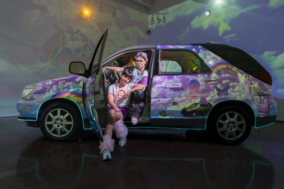 Liz Ferrer and Bow Ty, known as LIZN’BOW, pose in front of the car that is part of their exhibit “Niñalandia Skycoaster” at Miami’s Locust Projects.
