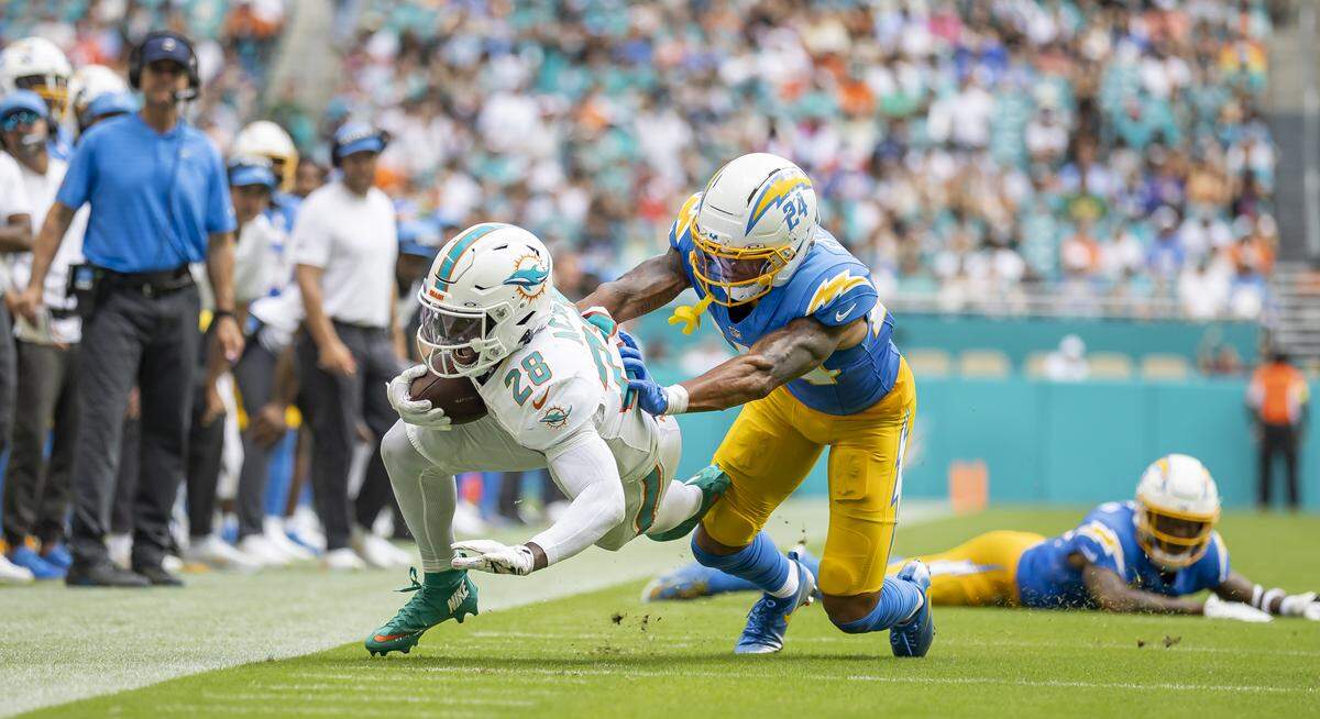 Miami Dolphins running back De'Von Achane (28) runs with the ball as Los Angeles Chargers cornerback Benjamin St-Juste (24) tackles him in the first half of their NFL game at Hard Rock Stadium on Sunday, Oct. 12, 2025, in Miami Gardens, Fla.