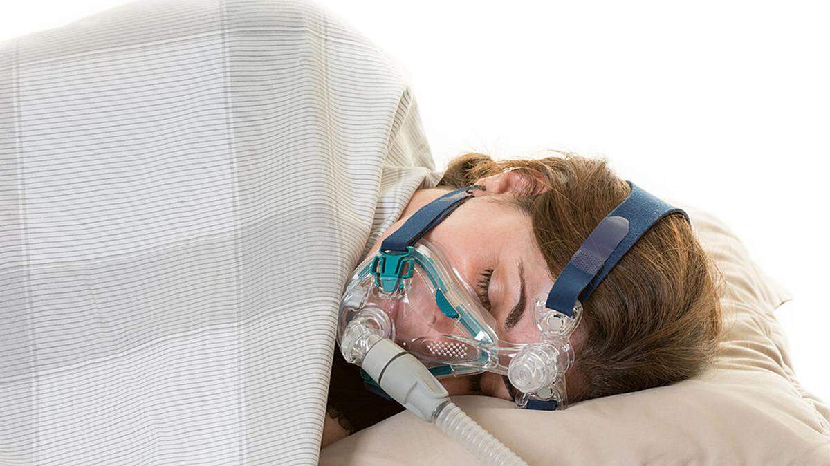 A woman wears a CPAP mask for treating sleep apnea, which is a type of sleep disorder characterized by pauses in breathing or instances of shallow or infrequent breathing during sleep.