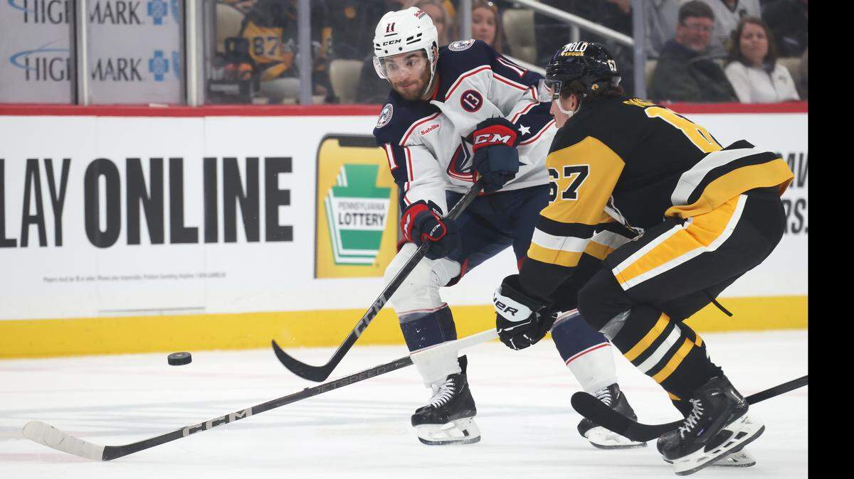 Mar 21, 2025; Pittsburgh, Pennsylvania, USA;  Columbus Blue Jackets center Luke Kunin (11) shoots the puck against Pittsburgh Penguins right wing Rickard Rakell (67) during the second period at PPG Paints Arena. Mandatory Credit: Charles LeClaire-Imagn Images