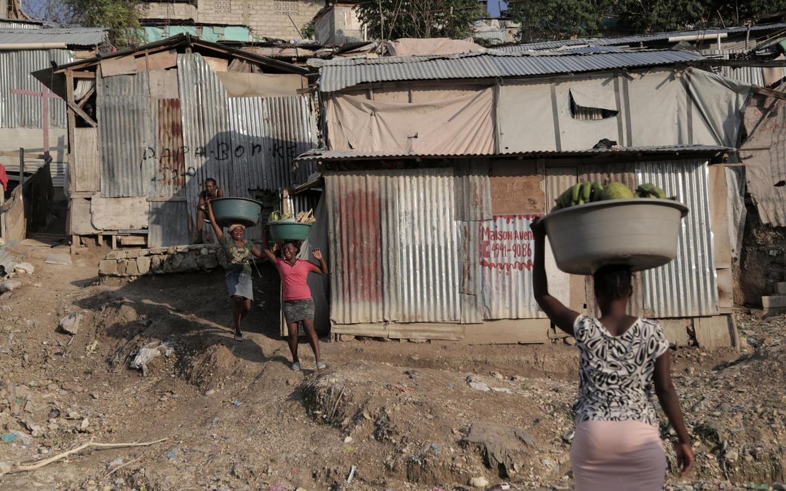 Women carrying produce and other goods walk by some of the tin shacks that make up the Teren Toto camp in Haiti’s capital.