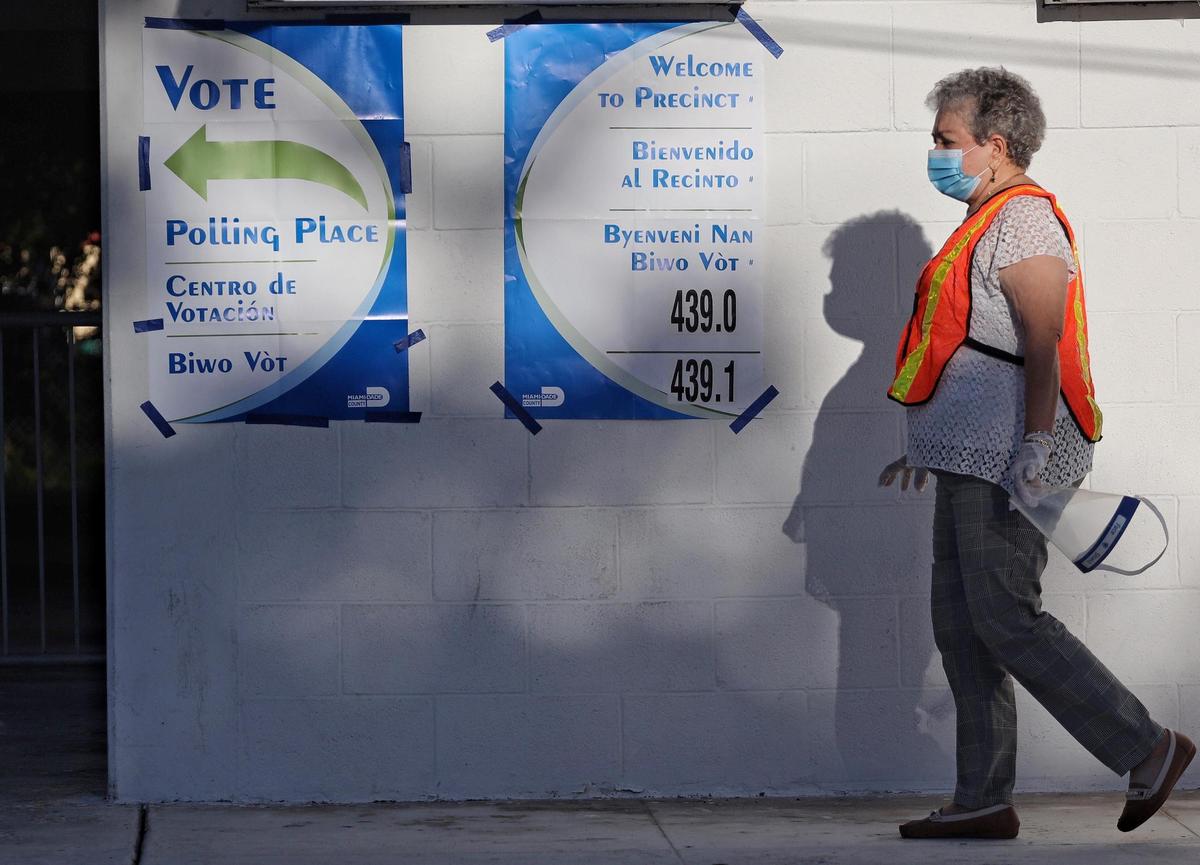 Retiree and volunteer poll worker Zeida Mesa, 83, walks pass the entrance of a poll site wearing proper PPE while assuring all voters wear masks in the Westchester area of Miami-Dade county on Primary voting Tuesday, Aug. 18, 2020.