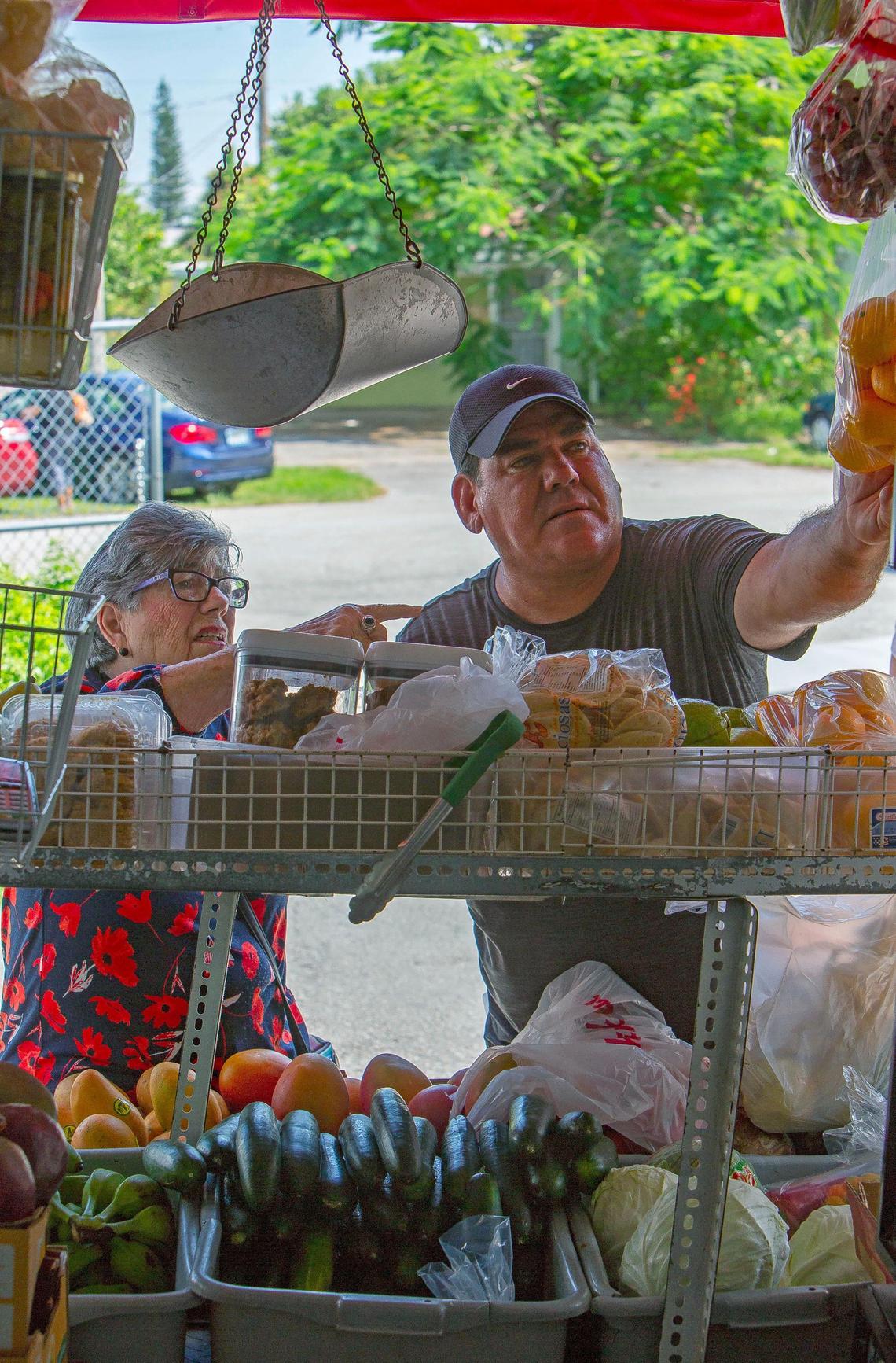 Bodega truck owner, Arturo Tamayo, helps a shopper reach some oranges as she goes through her shopping list in Miami, FL, on Wednesday, June 20, 2018.