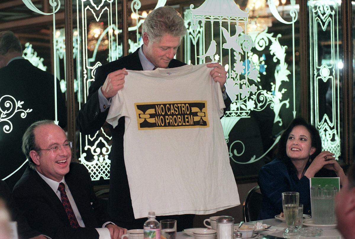 President Clinton holds-up a T-shirt that was given to him during a dinner at Little Havana restaurant Versailles, where several gathered to eat with the president in November 1996. On his left, Paul Cejas and at right, Maria Arias Rodham.