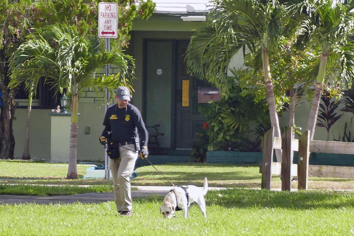 An ATF officer, with his police dog, checks out the area where the bloody body of a man was found at Scott Park in Miami Gardens on Nov. 2, 2018.