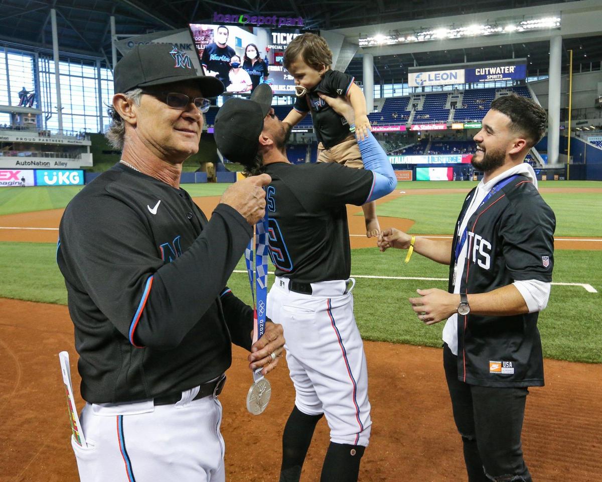 Miami Marlins manager Don Mattingly (8) holds Miami Marlins minor league shortstop Eddie Alvarez’s Olympic silver medal as shortstop Miguel Rojas (19) lifts, Alvarez’s baby, Jett Alvarez, before baseball game against the Chicago Cubs at loanDepotPark in Miami on Friday, August 13, 2021.