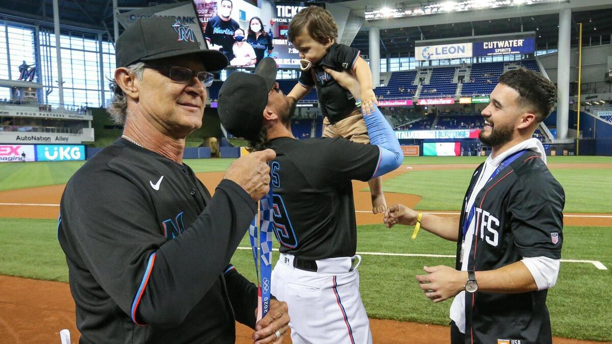 Miami Marlins manager Don Mattingly (8) holds Miami Marlins minor league shortstop Eddie Alvarez’s Olympic silver medal as shortstop Miguel Rojas (19) lifts, Alvarez’s baby, Jett Alvarez, before baseball game against the Chicago Cubs at loanDepotPark in Miami on Friday, August 13, 2021.