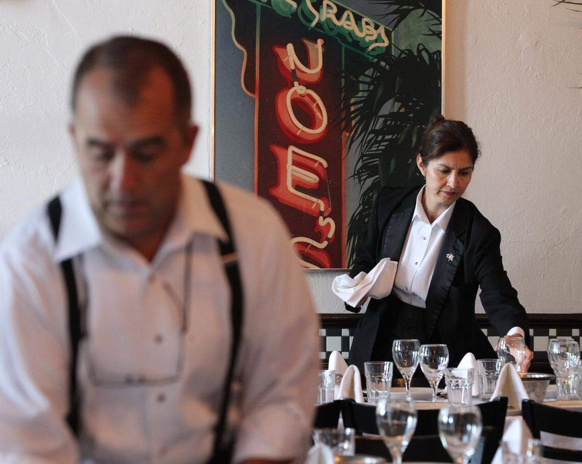 Server Lorena Garcia (at right) sets up her table on Monday October 14, 2013 as Joe’s Stone Crab reopens and celebrates its 100th anniversary. The restaurant, with an occupancy of 400 people in its dining room, is one of the clubs and restaurants affected by a new coronavirus emergency order from the City of Miami Beach limiting occupancy at big venues.