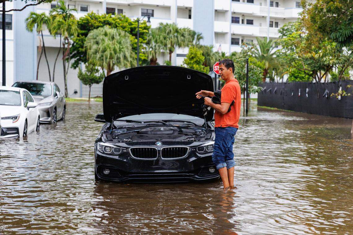 A man stands next to his vehicle stranded on the road flooded due to heavy rain at North Bay Road and 179th Drive in Sunny Isles Beach on Wednesday, April 25, 2023.