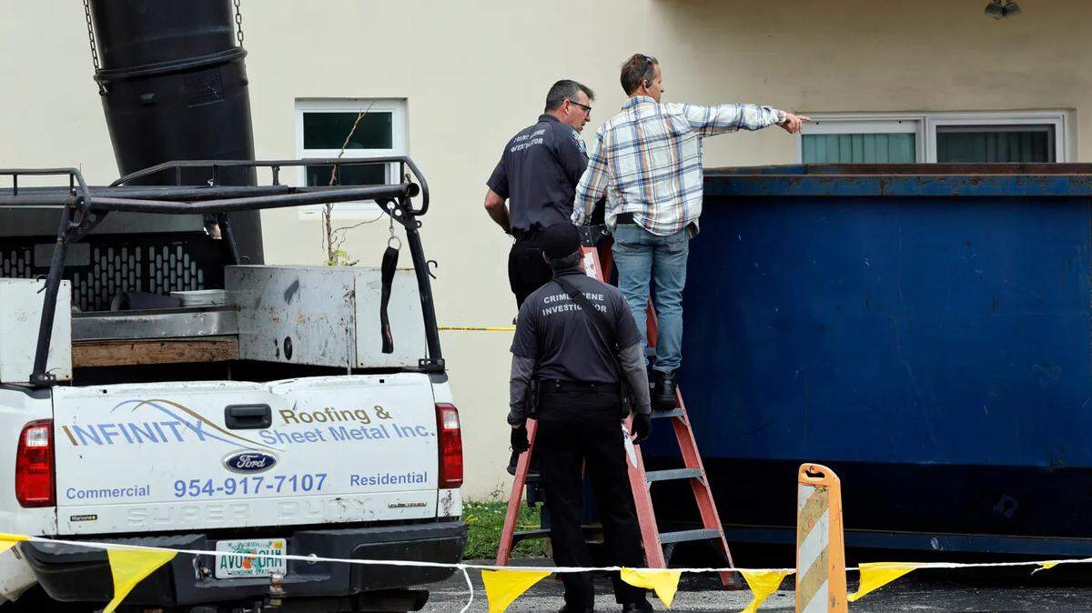 A man standing with a crime scene investigator points to the inside of a large trash bin outside of an apartment complex in Hollywood where construction workers found a dead baby on Monday. (Amy Beth Bennett / South Florida Sun Sentinel)