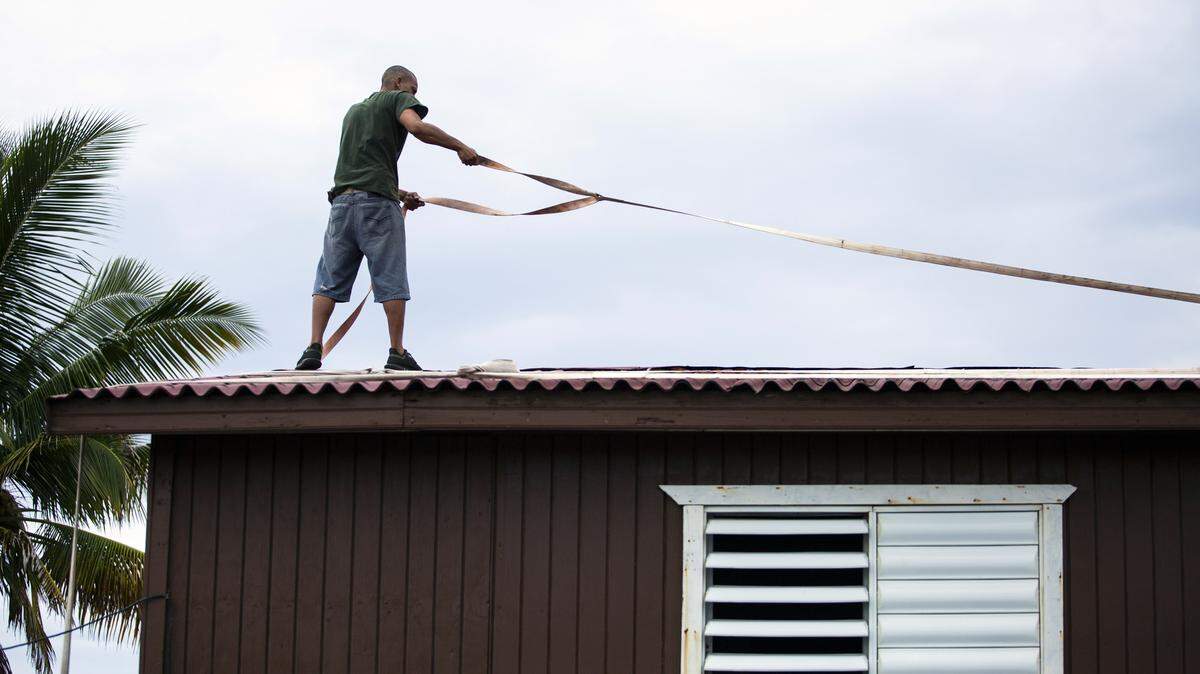 A man uses straps to tie down the roof of his home in Yabucoa, Puerto Rico, as Dorian approaches on Wednesday, Aug. 28, 2019. By 2 p.m., the tropical storm had strengthened to a hurricane.