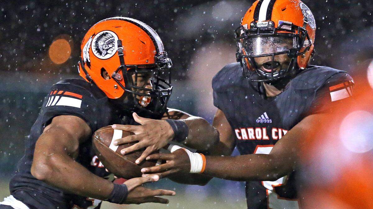 Carol City High’s quarterback Daniel Richardson hands-off to Katravis Geter, (3), in the first quarter during a rain storm as Columbus plays against Carol City in football at Traz Powell Stadium on Friday, September 7, 2018.