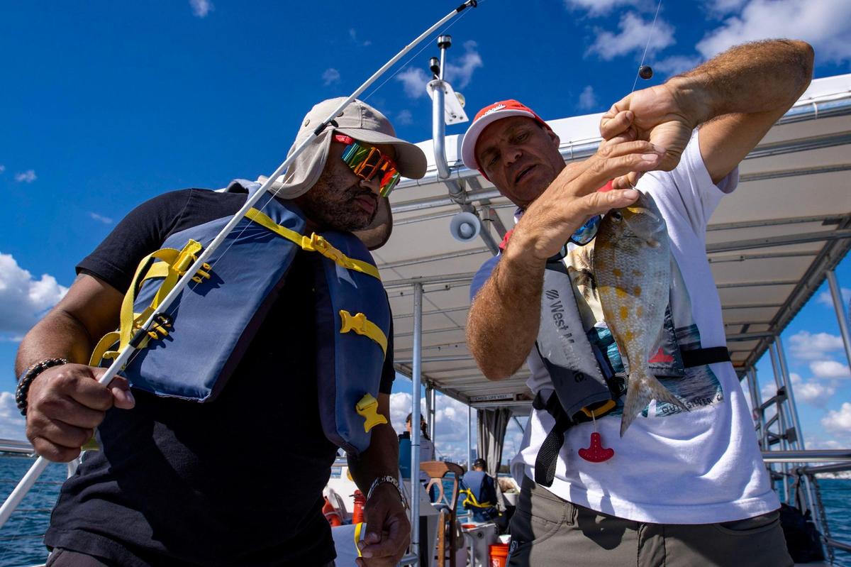 El veterano militar René Segura aprende a desenganchar un pez del capitán Emiliano de Shake-A-Leg Miami, durante una salida de pesca como parte del programa para veteranos de Shake-A-Leg, en la Bahía de Biscayne el 12 de enero de 2023. Segura, recién llegado de Nueva York, nunca había pescado antes de esta salida.