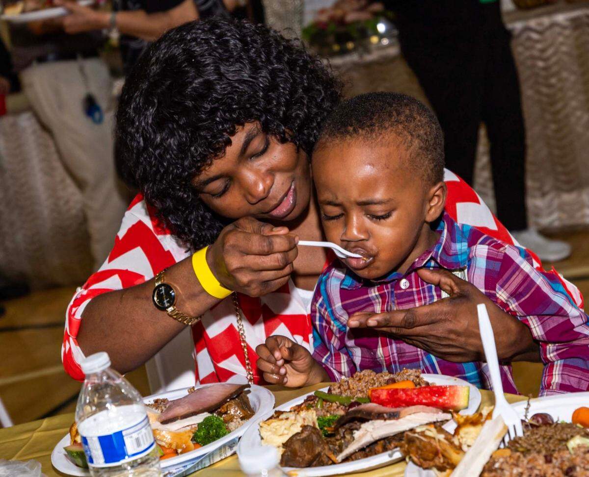 A mother feeds her son during the 18th Annual Haitian Thanksgiving Brunch.