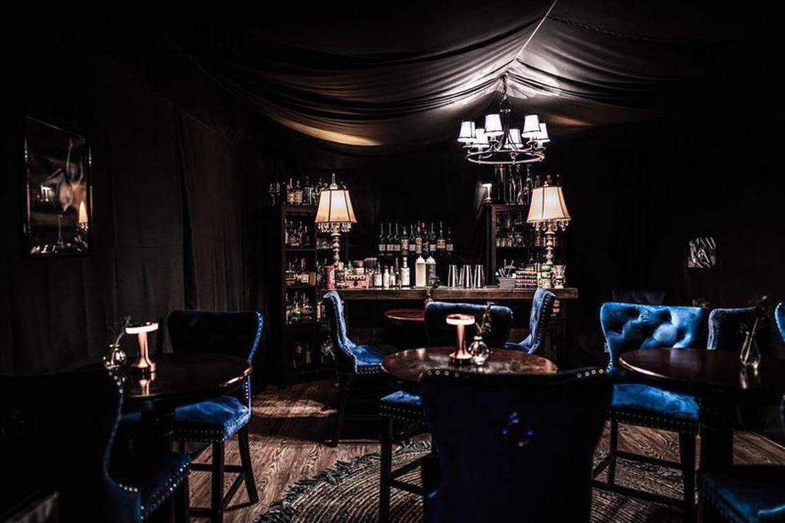 Dark paneling and navy velvet upholstery create a dark, lush atmosphere at Room 901, a guest room turned speakeasy at the Hyatt Centric Las Olas.